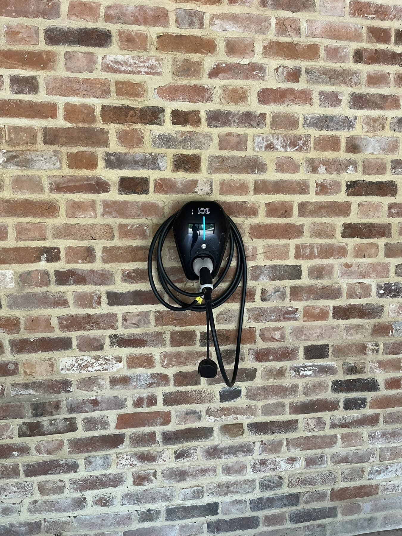 Black EV charge point mounted on a brick wall with the charging lead hung neatly beneath it