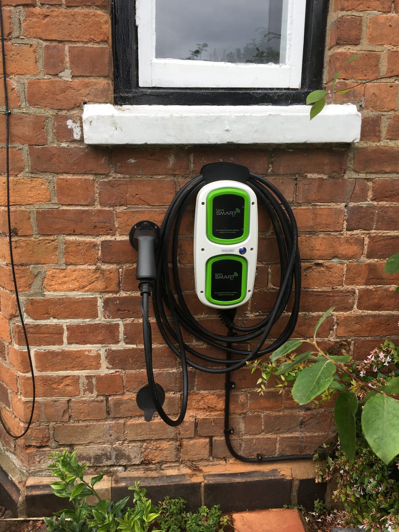 Wall mounted EV charge point fitted to the red brick wall of a cottage with the cable coiled neatly on the holster