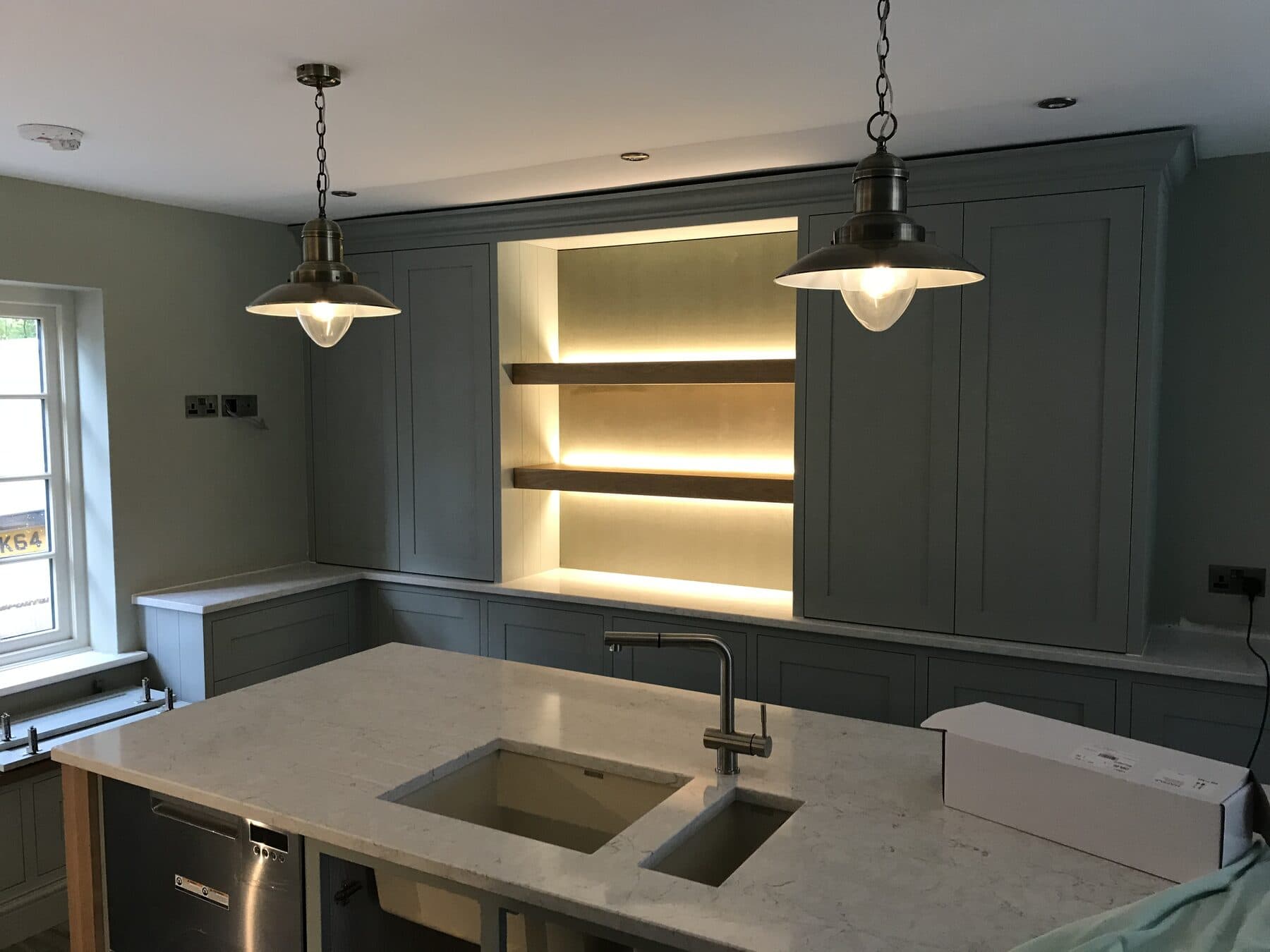 Shaker kitchen with glass pendant lights over a stone island and warm LED strip lighting behind open oak shelves