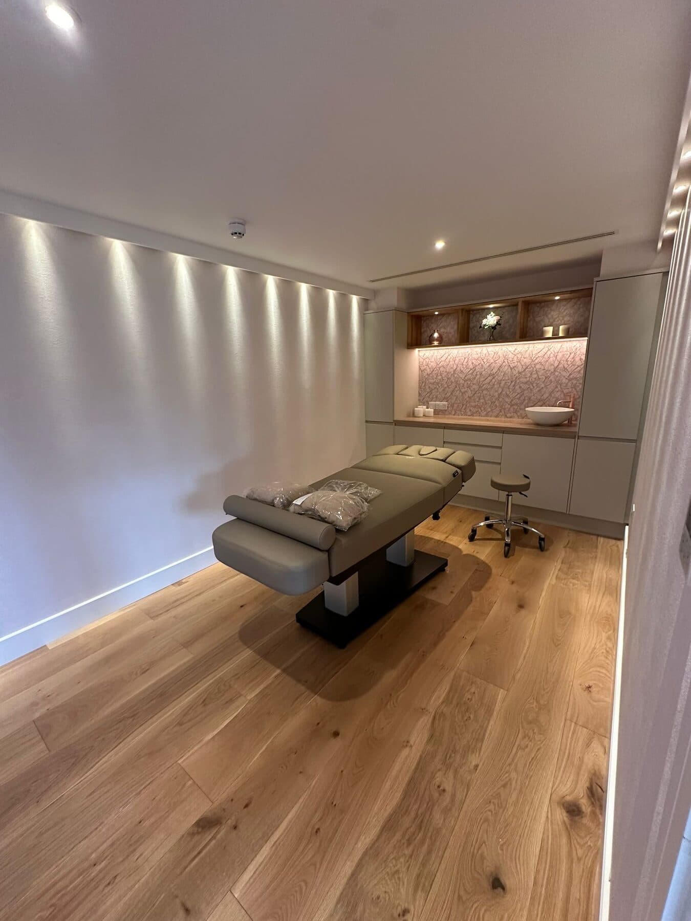Treatment room lit end to end by concealed wall wash lighting, with a lit display alcove beside the basin